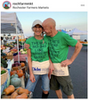 Two people smiling and standing close together at a farmers market, wearing matching green union labor t-shirts that read, There’s no day like farmers market day.