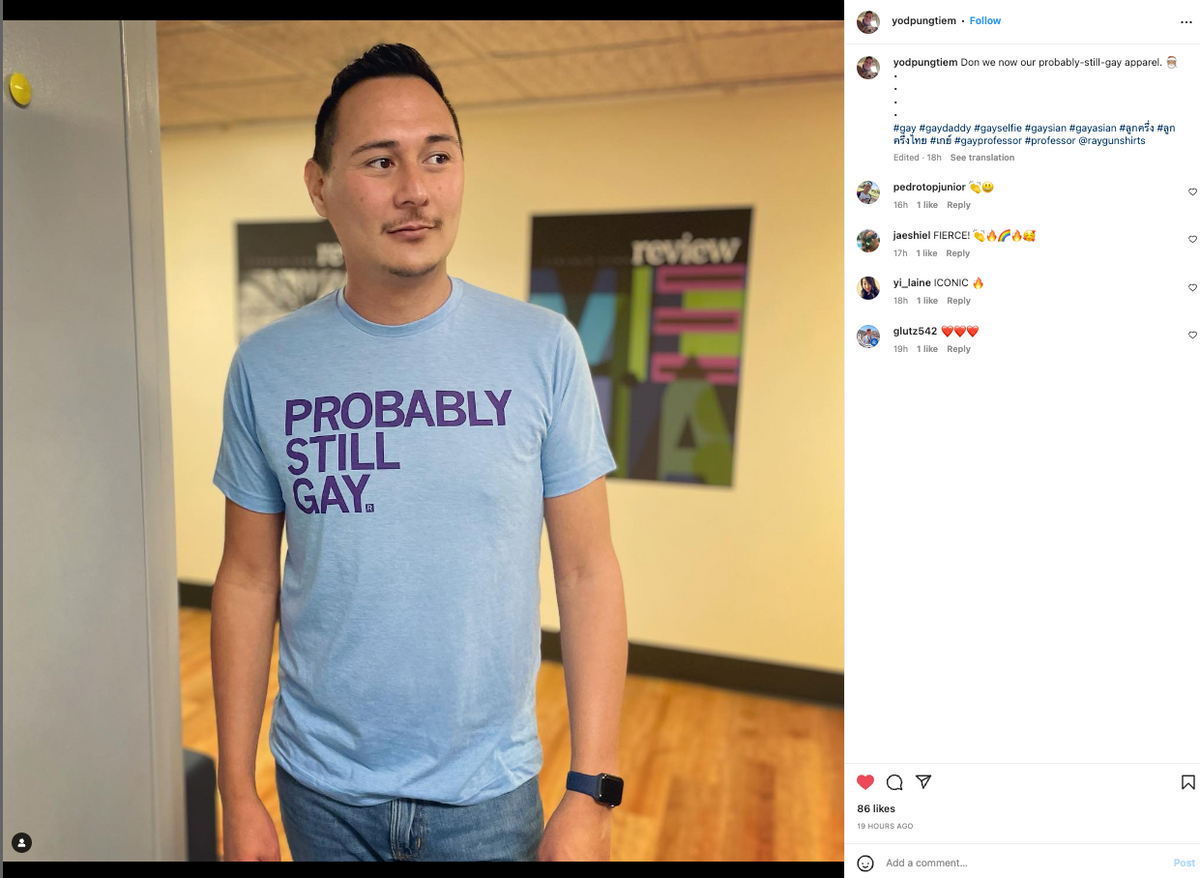 A man wearing a light blue, union-made RAYGUN t-shirt with the text PROBABLY STILL GAY. printed on the front.