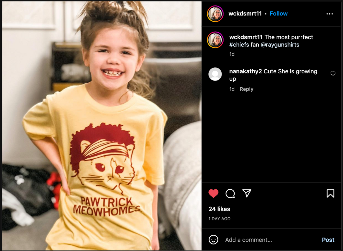A smiling young girl wears a yellow, union-made cat t-shirt featuring a cartoon cat wearing a red headband with the text PAWTRICK MEOWHOMES.
