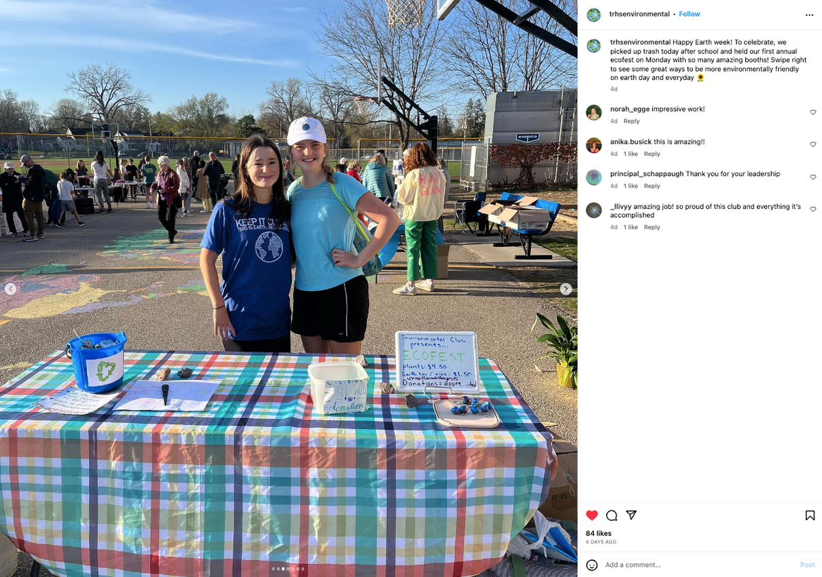 Two young women in union made, eco-friendly t-shirts stand behind a booth for an Iowa Environmental Council event, featuring a sign detailing plants for sale and donations.