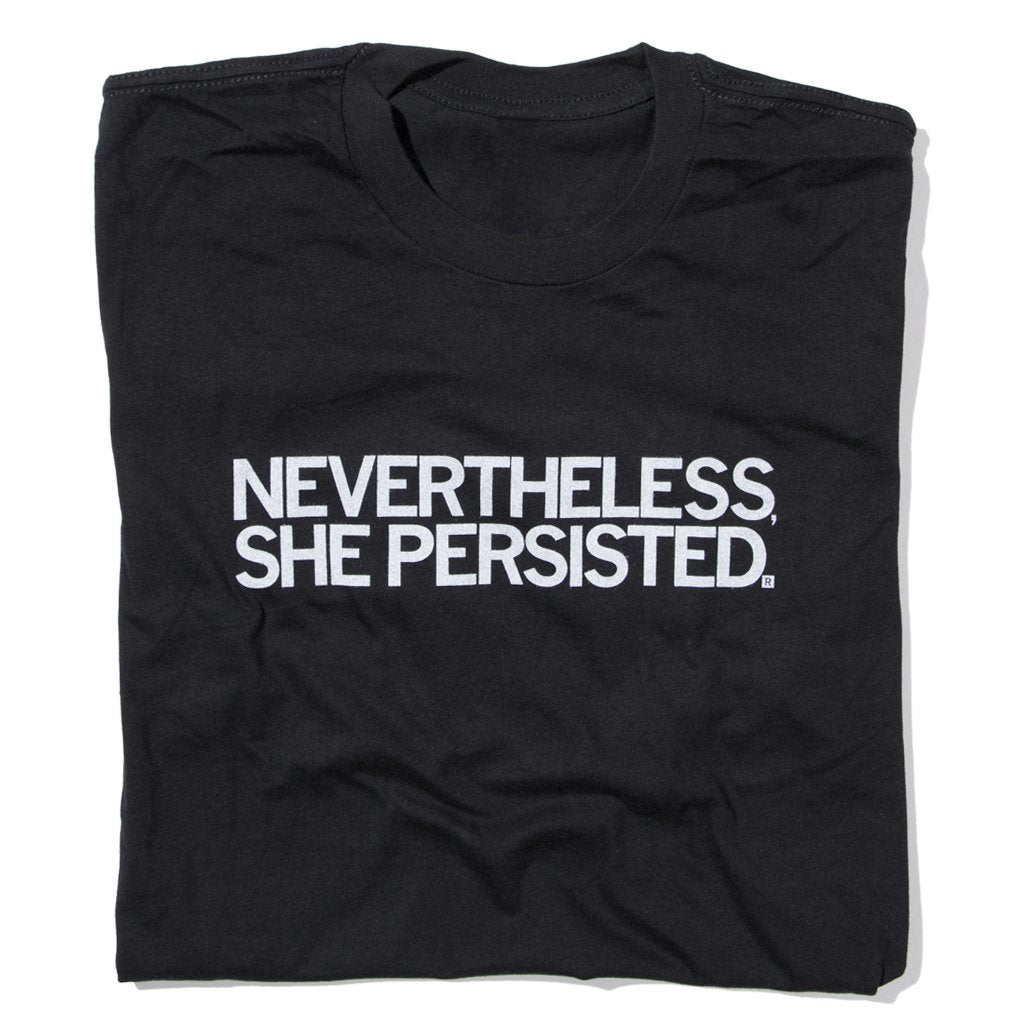 A folded black t-shirt with white ink text that reads "Nevertheless, She Persisted"