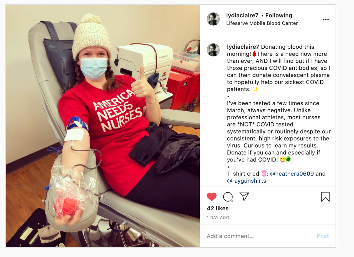 A person in a beanie and face mask sits in a donation chair giving a thumbs up while donating blood, wearing a red t-shirt that says AMERICA NEEDS NURSES as a symbol of union labor.
