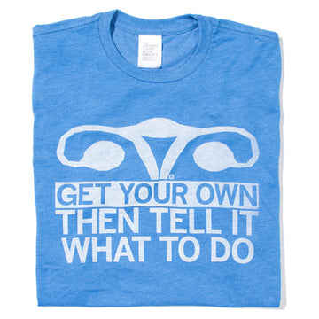 Folded heather blue shirt with in illustration of a uterus in white ink and text below that says, "Get Your Own, Then Tell It What To Do!"