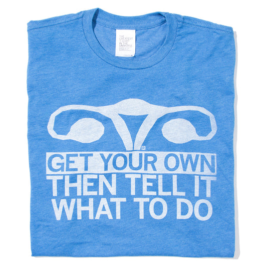 Folded heather blue shirt with in illustration of a uterus in white ink and text below that says, "Get Your Own, Then Tell It What To Do!"