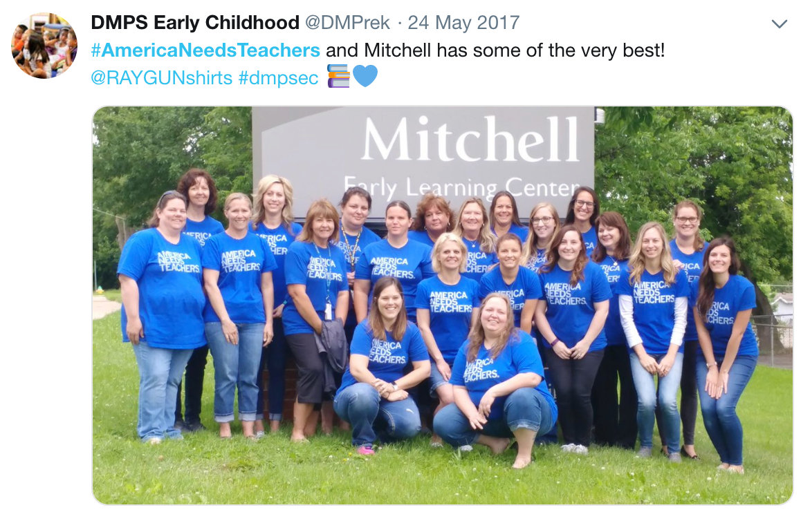 A large group of teachers posing in front of the Mitchell Early Learning Center sign, all wearing matching union made blue t-shirts that say America Needs Teachers to show their support for public education.