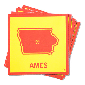 A stack of square vinyl stickers featuring an outline of Iowa in red on a yellow background, with a yellow asterisk marking Ames and the city name printed below.