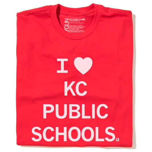 A red RAYGUN t-shirt with white text that reads I [heart symbol] KC PUBLIC SCHOOLS.