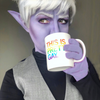 A person in purple elf-like cosplay makeup holds a fade resistant white mug with rainbow text that reads, THIS IS PRETTY GAY.