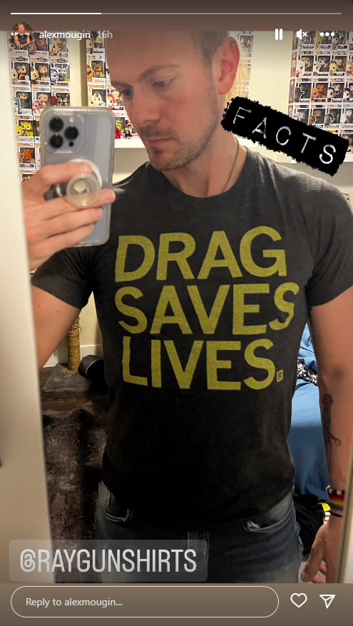 A man taking a mirror selfie in a charcoal t-shirt that says DRAG SAVES LIVES in yellow letters.