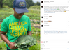 A smiling person in a baseball cap and a heather kelly green t-shirt that reads America Needs Lesbian Farmers holds a large bunch of kale in a field.