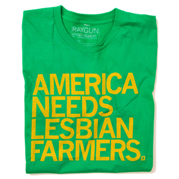A folded heather kelly green shirt with left aligned yellow text that says, "America Needs Lesbian Farmers"