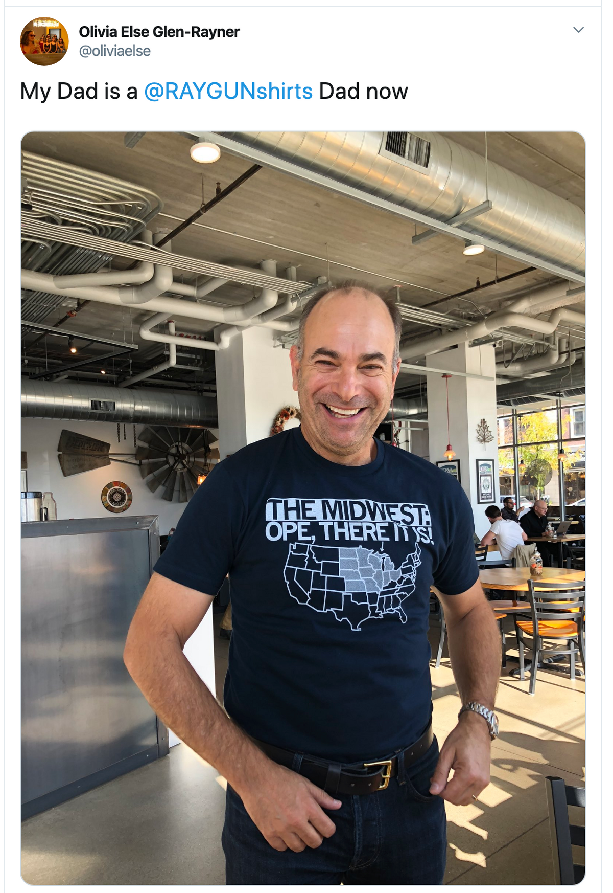 A smiling man wears a navy blue RAYGUN Midwest T-shirt featuring a map of the United States with the region highlighted and the text THE MIDWEST: OPE, THERE IT IS!.