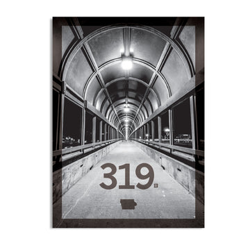 Black and white photo of a covered pedestrian bridge looking down a long, arched tunnel, with the 319 Iowa area code and the state’s shape printed in the foreground.
